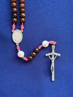 --- 1" St. Agatha/pink ribbon rosary center --- 1 7/8" Papal crucifix --- 10mm hand painted pink ribbon Our Father beads --- 8mm natural Madre de cacao wood Hail Mary beads --- stainless steel accent spacers --- pink micro cord  --- lightweight and approximately 17 inches long Please let us know, if you have any questions. Follow us on Instagram and Facebook @sistersinchristrosaries to see our latest designs. Please note that colors may differ slightly from how they appear on your screen due to varying monitor settings. Also, due to the nature of natural wood beads and gemstones, variety in wood grain pattern and coloration is to be expected. Adjustable Pink Cross Rosary, Handmade Pink Rosary With Cross Shape, Handmade Pink Rosary In Cross Shape, Handmade Pink Rosary With Cross, Handmade Pink Cross Rosary, St Agatha, Saint Agatha, Our Father, Hail Mary