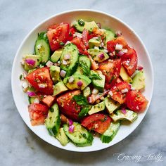 a white bowl filled with cucumber, tomato and onion salad on top of a marble table