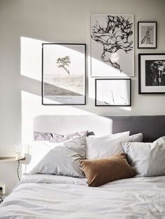 a bed with white sheets, pillows and pictures on the wall above it in a bedroom