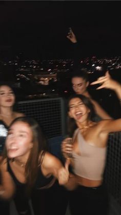 four women are posing for the camera in front of a cityscape at night