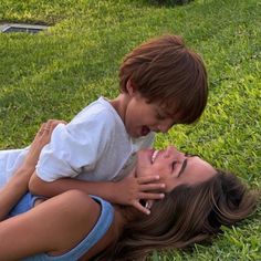 a woman laying in the grass with a child on her back and one hand over her mouth