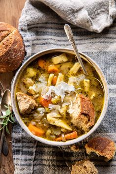 two hands holding a bowl of soup with bread on the side