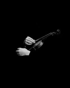 black and white photograph of a person holding a violin in their right hand with both hands