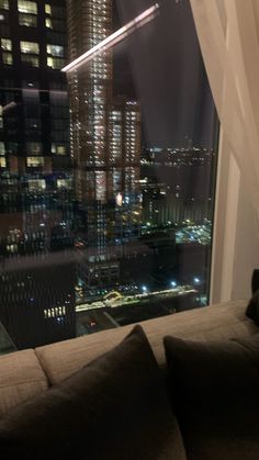 a couch in front of a window overlooking a cityscape at night with the lights on