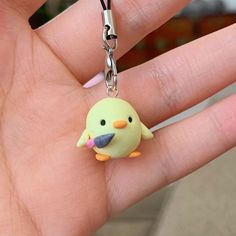 a hand holding a tiny yellow bird keychain on it's thumb,