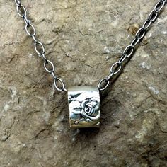 a silver necklace on a rock with a small square pendant hanging from it's center