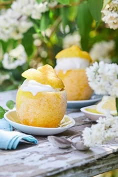 two lemon muffins sitting on top of a wooden table next to white flowers