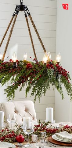 a chandelier hanging over a dining room table decorated with greenery and candles