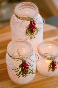 three mason jars with red berries are sitting on a wooden table next to some candles