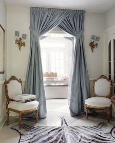 a living room with two chairs and a rug in front of a window that has blue drapes on it