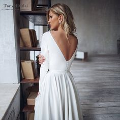 a woman in a white dress leaning against a bookshelf with her back to the camera