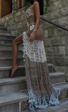 a woman is sitting on the steps wearing a crochet dress