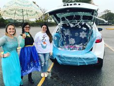 three women standing next to an open car trunk with snowflakes on the hood