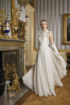 a woman in a white wedding dress standing next to a fire place with her hands on her hips