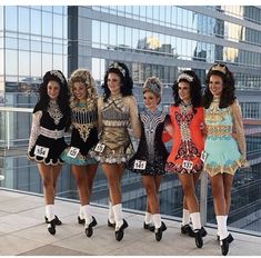 four women dressed in costumes posing for a photo on the roof of a skyscraper building