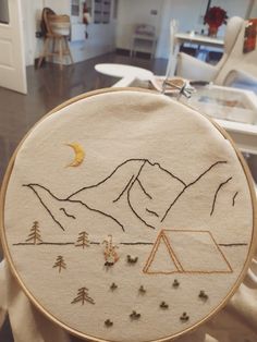 a hand embroidered camper's tent with mountains and trees in the background on a table