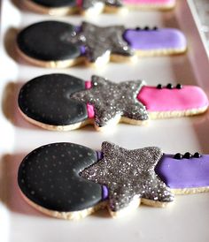 decorated cookies with black, pink and purple icing are lined up on a white tray