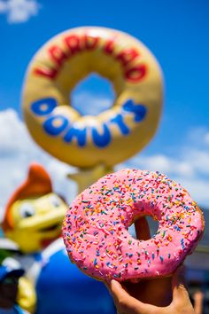 a person holding up a doughnut with sprinkles in front of a sign