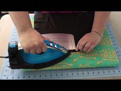 a person cutting fabric with scissors on top of a table next to an ironing board