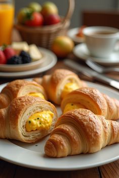 croissants with eggs and cheese are on a white plate next to fruit