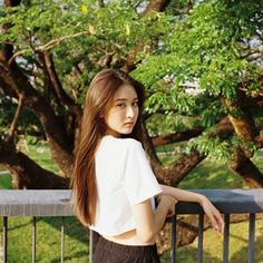 a young woman standing on a balcony next to a tree and looking off into the distance