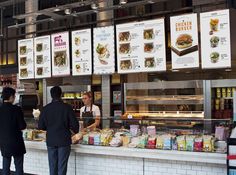 people standing in line to order food from the counter at a fast food restaurant with menus hanging on the wall