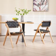 two wooden chairs sitting next to each other near a table with a vase on it