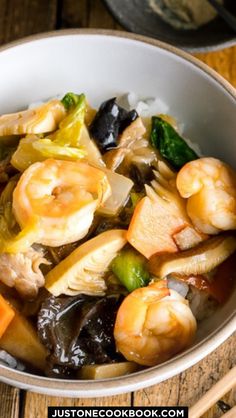 shrimp and vegetable stir fry in a bowl with chopsticks next to it on a wooden table