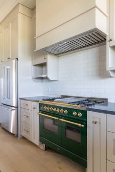 a green stove top oven sitting inside of a kitchen next to white cabinets and drawers