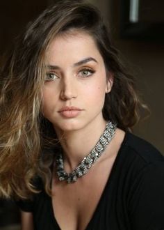 a woman with long hair wearing a black shirt and silver necklace, looking at the camera