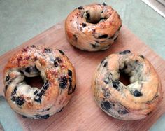 three blueberry bagels sitting on top of a wooden cutting board