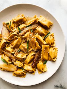 a white plate topped with pasta and meat covered in sauce on top of a marble table