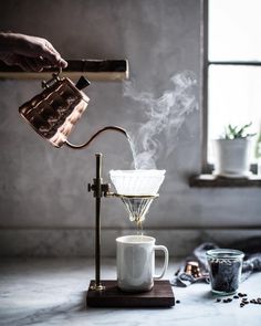 a person pours coffee into a cup with steam coming out of the filterr