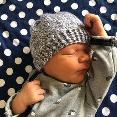 a baby wearing a knitted hat laying on top of a polka dot blanket with it's eyes closed