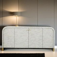 a white and gold sideboard with a lamp next to it on the floor in front of a wall