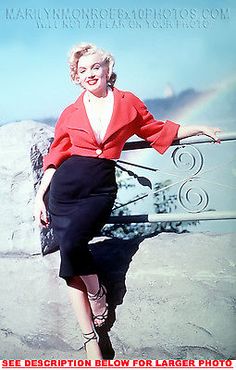 a woman in a red shirt and black skirt leaning on a fence with her arms outstretched