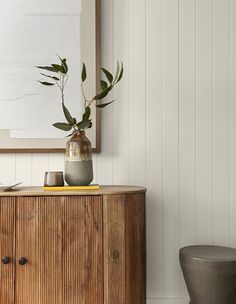 a wooden cabinet sitting next to a vase with plants in it on top of a rug