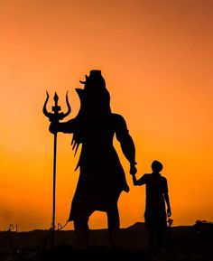 the silhouette of a man and woman standing next to a giant statue in front of an orange sky