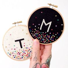 someone is holding up two small embroidered hoops with the letter m on each one