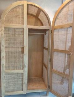 an open wooden cabinet sitting on top of a tiled floor next to a wall with two arched doors