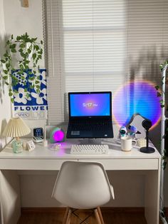 a laptop computer sitting on top of a white desk next to a lamp and window