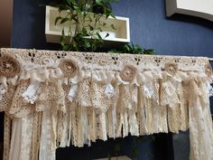 an old lace curtain with flowers hanging from it's side in front of a blue wall