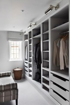 a walk in closet filled with lots of white shelves and clothes on top of them