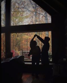 two people standing in front of a window with the sun shining on them and trees outside