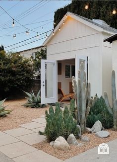 a small white house with cactus plants in the front yard and lights strung above it