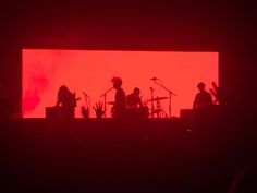 silhouettes of band members on stage with red light in the backgrouund