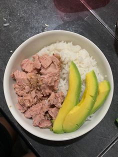 a white bowl filled with meat and rice next to avocado slices on a counter