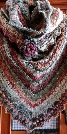 a multicolored crocheted shawl draped over a window sill in front of a wooden door