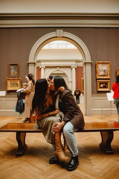 two women sitting on a bench in an art gallery kissing each other's noses