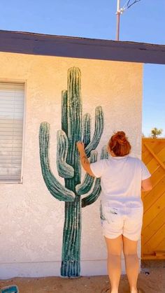 a woman painting a cactus on the side of a house